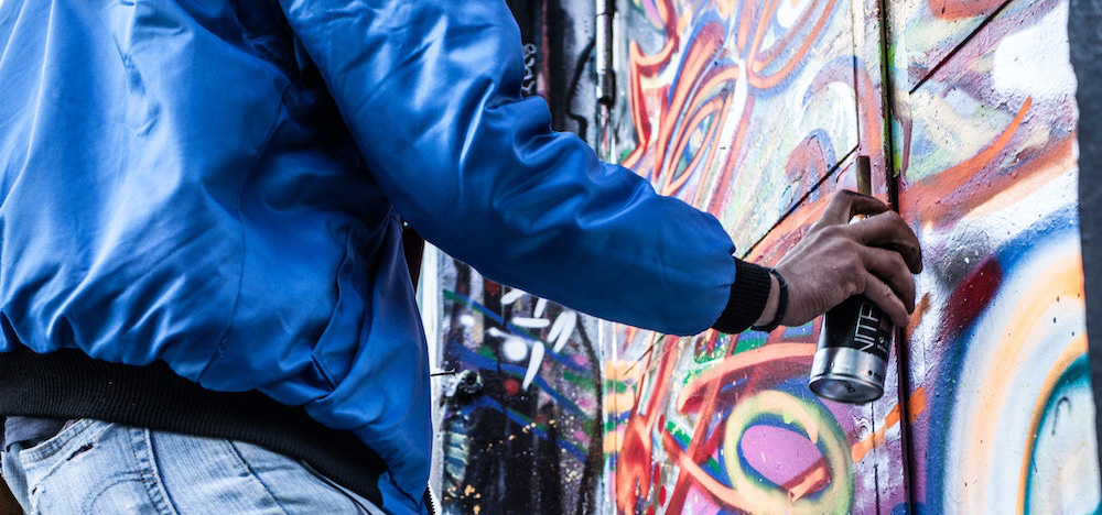 Ein Streetartist sprüht Farbe auf eine bunte Wand.