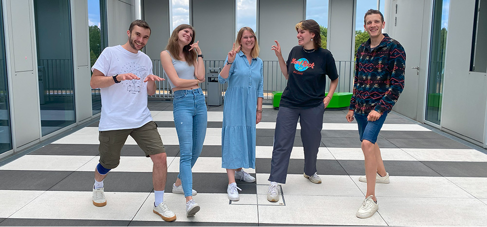 Ein Foto mit den Autoren des Bloges. Sie stehen in einem Innenhof der Hochschule der Medien und lachen in die Kamera.